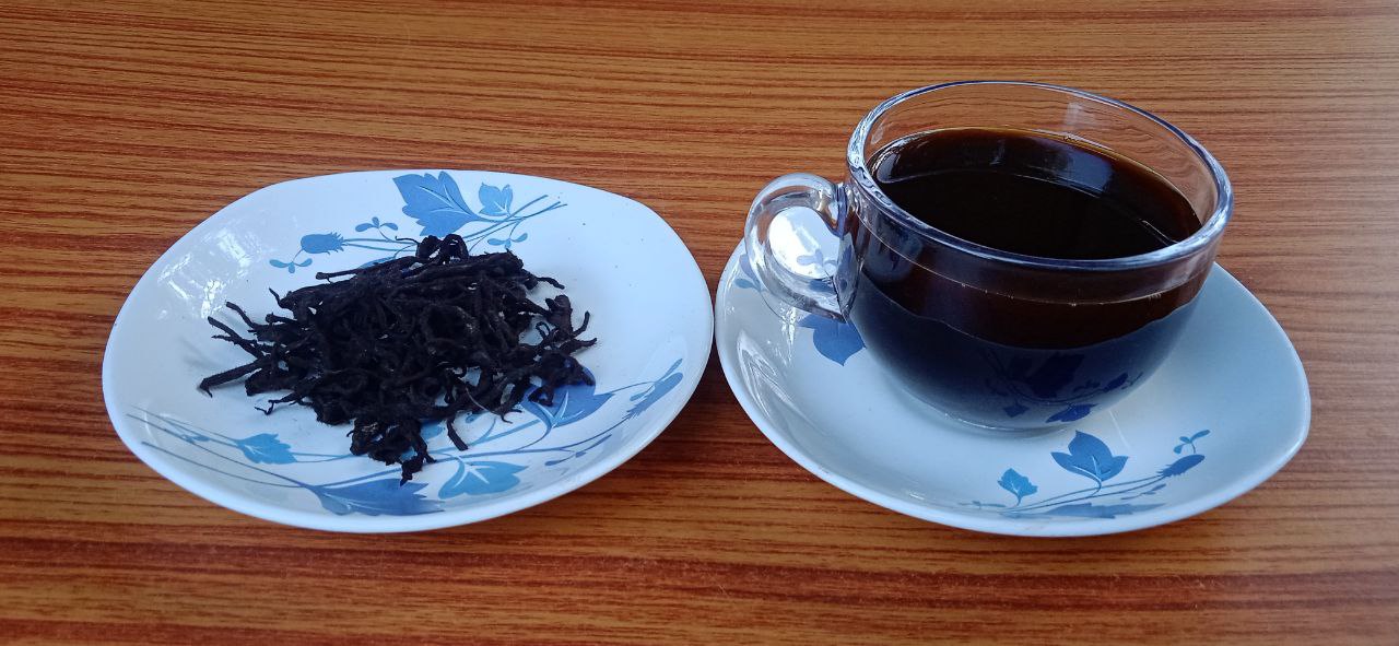 A cup of steaming black tea next to a plate of loose black tea leaves, showcasing their dark, wiry texture.